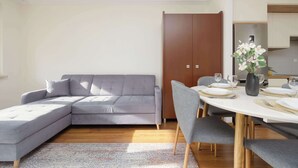 Ein modernes Wohnzimmer mit einem grauen Ecksofa, einem Esstisch für vier Personen und einem Holzschrank.