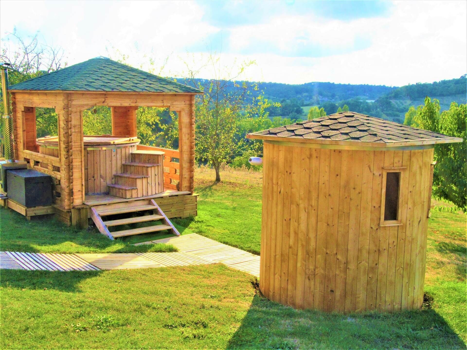 A wooden cabin with a porch and a hot tub, surrounded by a grassy yard and trees.