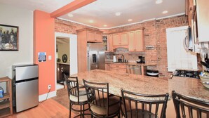 A kitchen with granite countertops, a stainless steel refrigerator, and a brick wall.