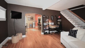 A living room with a white couch, a bookshelf, a TV mounted on the wall, and a staircase leading to another level.