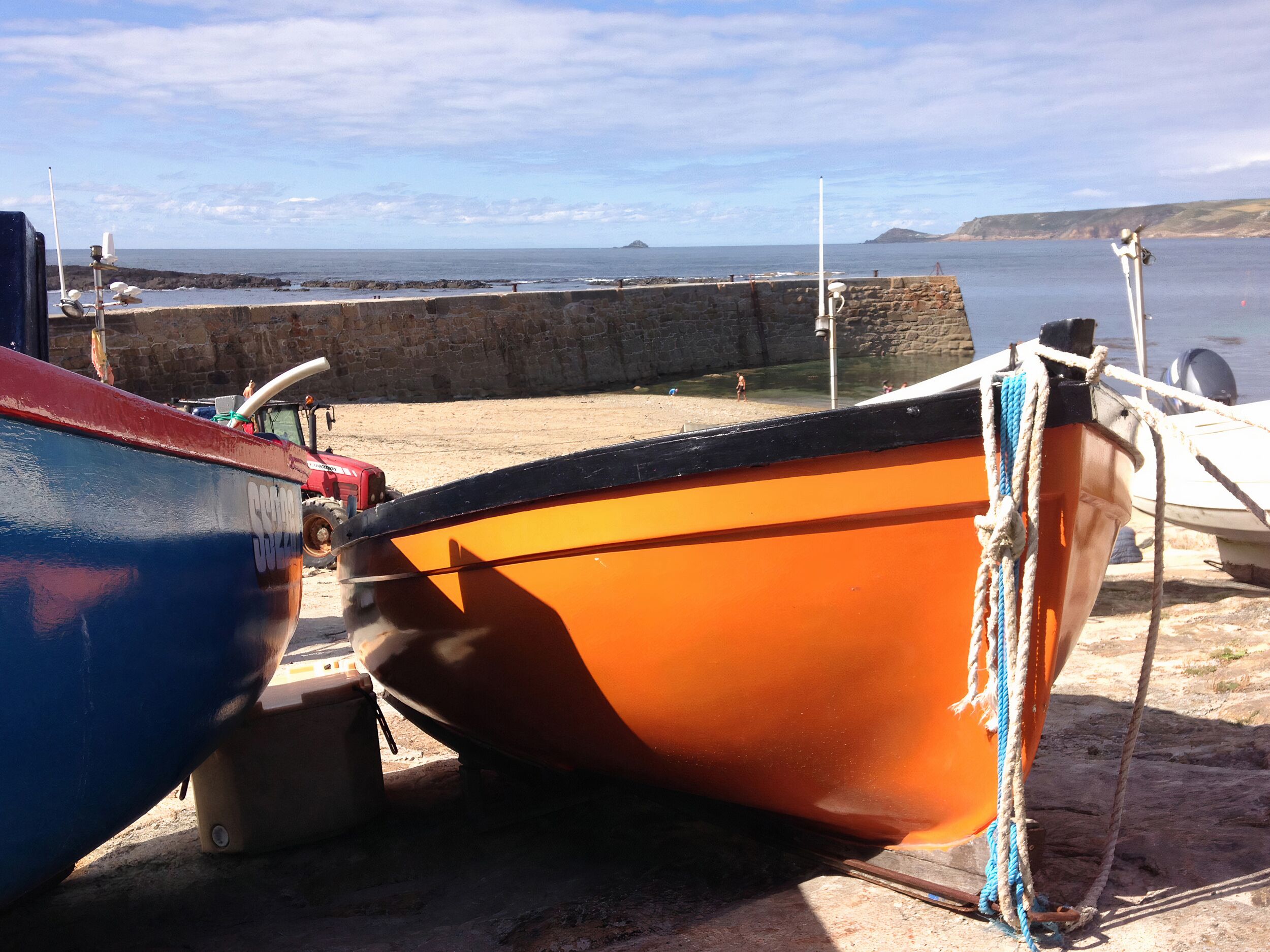 Boats docked at a pier with a stone wall and a view of the sea and distant land.