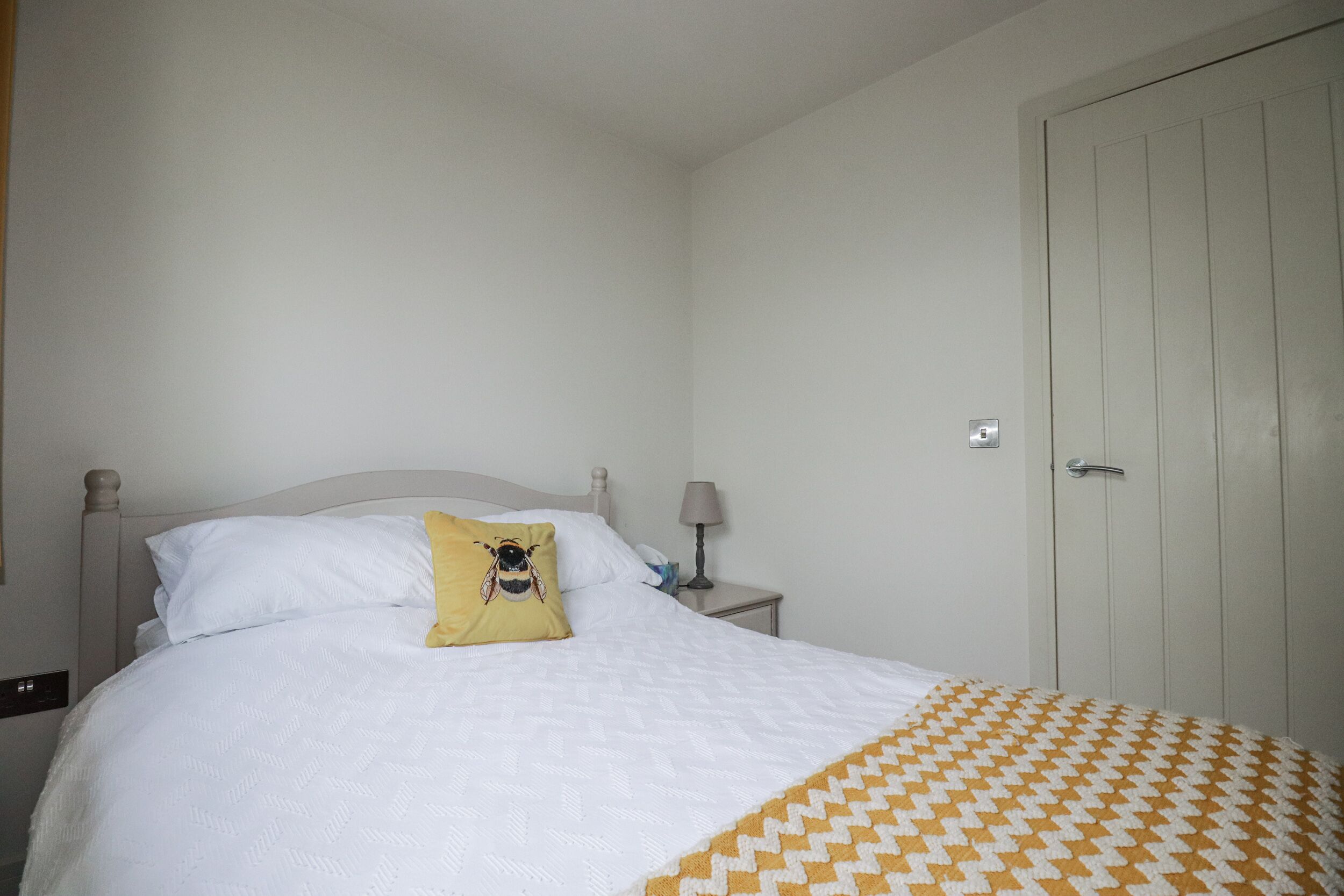 A neatly made bed with a yellow pillow, a white quilt, and a patterned blanket.