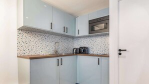 A compact kitchen with light blue cabinets, a stainless steel sink, and a microwave. - 11 Beaumarchais 5D (Paris)