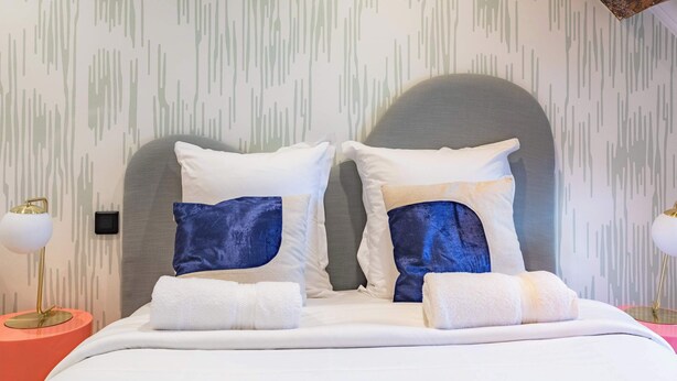 A bed with white bedding, two pillows with a blue accent, and a grey headboard. - 11 Beaumarchais 5D (Paris)