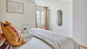 A hotel room with a bed, a map on the wall, a window with curtains, and a mirror.