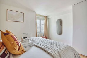 A hotel room with a bed, a map on the wall, a window with curtains, and a mirror.
