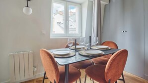 A dining area with a table set for four, a window with a view of buildings, and a radiator on the wall.