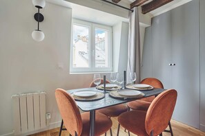 A dining area with a table set for four, a window with a view of buildings, and a radiator on the wall.