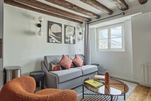 A modern living room with a grey sofa, orange armchair, and a glass coffee table.