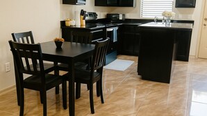 Een moderne keuken met zwarte kasten, een eettafel met vier stoelen en een klein aanrecht met een spoelbak.