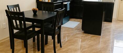 Une cuisine moderne avec des meubles de rangement noirs, une table à manger avec quatre chaises et un petit îlot central doté d’un évier.
