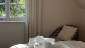 Ein Zimmer mit einem Bett, einem Fenster und einem Korbstuhl.