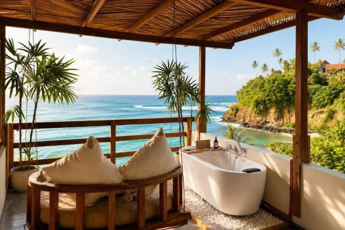 A balcony with a view of the ocean, a bathtub, and a wooden chair with cushions.