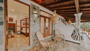 A room with a stone wall, wooden ceiling beams, wicker chairs, and a hanging light fixture. - Ocean Bliss by Sugar Coliving (Matara)