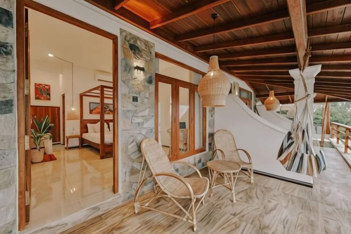 A room with a stone wall, wooden ceiling beams, wicker chairs, and a hanging light fixture.