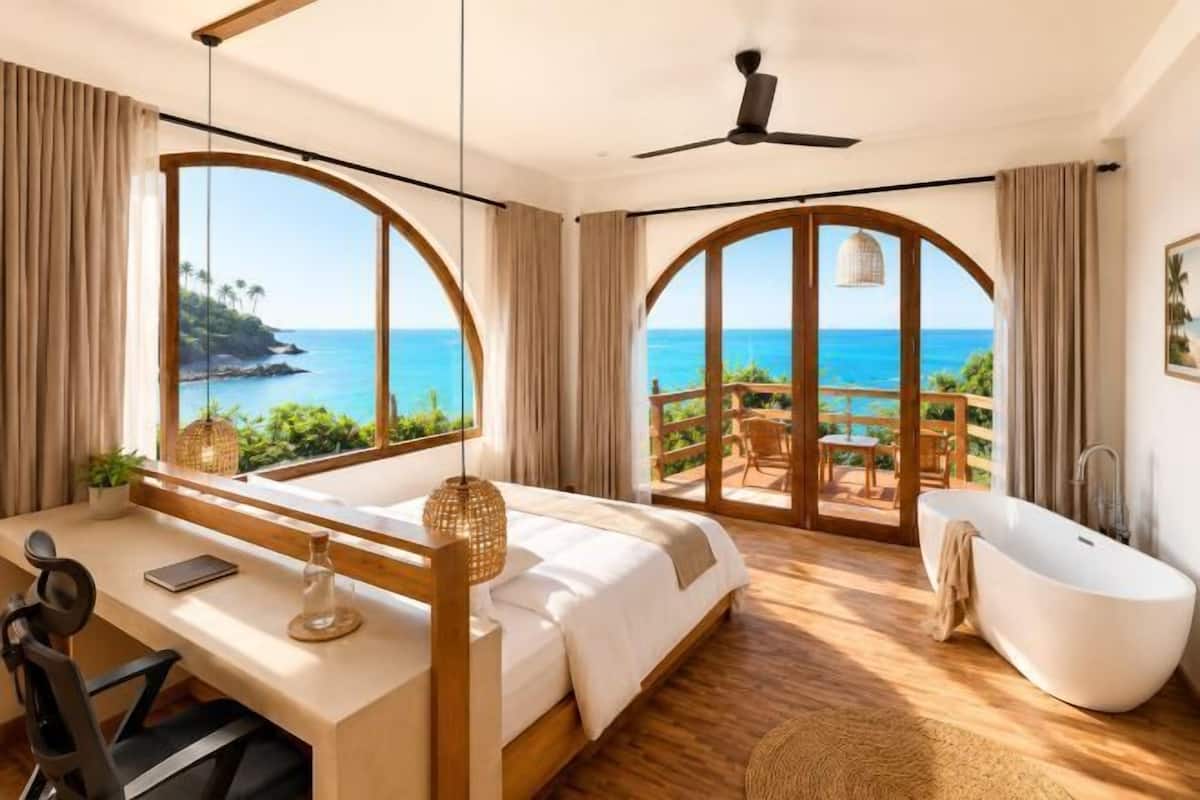 A bedroom with a large bed, a desk, a bathtub, and a view of the ocean.