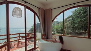 A room with a large bathtub, wooden furniture, and large windows with a view of the sea. - Ocean Bliss by Sugar Coliving (Matara)
