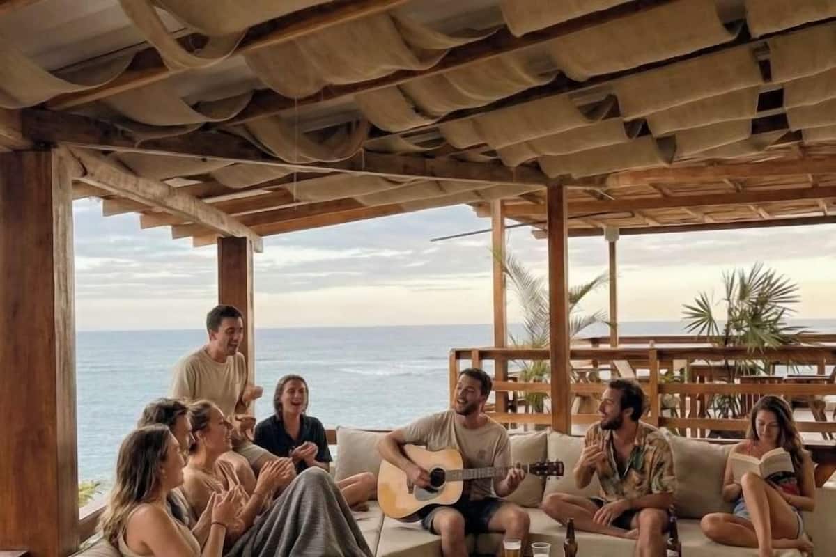 A group of people sitting on a couch under a wooden pergola with a view of the ocean.