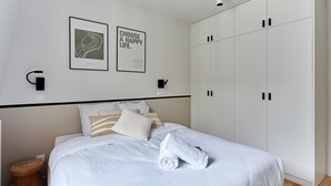 A bedroom with a bed, two wall-mounted light fixtures, a wardrobe, and two framed posters. - Large apartment Arc de Triomphe (Paris)