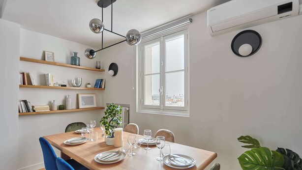 A dining area with a wooden table set for four, a potted plant, and a view of the city through a large window. - Large apartment Arc de Triomphe (Paris)