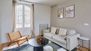 A living room with a sofa, a round table, a chair, a radiator, and two framed artworks on the wall. - Large apartment Arc de Triomphe (Paris)