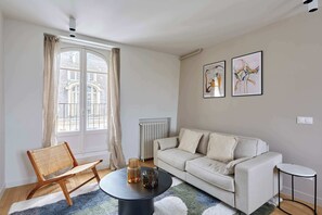 Ein Wohnzimmer mit einer Couch, einem runden Tisch, einem Sessel, einem Heizkörper und zwei gerahmten Kunstwerken an der Wand.