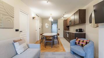 Een moderne keuken met houten kasten, een eethoek met een ronde tafel en stoelen, en een zithoek met een bank en fauteuil.
