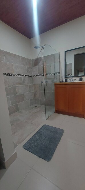 A modern bathroom with a glass-enclosed shower, a wooden vanity, and a large mirror. - "bosquelago" Houserental (Tronadora)