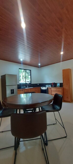 A modern kitchen with a wooden ceiling, a dining table with chairs, and a window providing natural light. - "bosquelago" Houserental (Tronadora)