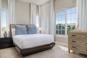 Ein Schlafzimmer mit Bett, Nachttischen, einem Schminktisch und großen Fenstern.