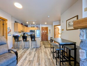 A modern kitchen with wooden cabinets, a stainless steel refrigerator, and a microwave. There are two bar stools and a wooden dining table with benches. - Mountain Escape  | Walk to Village & Summer Fun (Keystone)