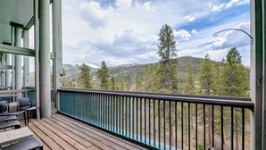 Una terraza de madera con mobiliario exterior, barandilla y vistas a un paisaje montañoso.