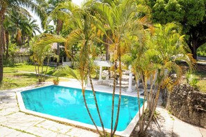 A rectangular swimming pool surrounded by palm trees and a stone wall. - Apartment with pool and view, minutes away from Cofresí and Costambar beaches. (Cofresi)