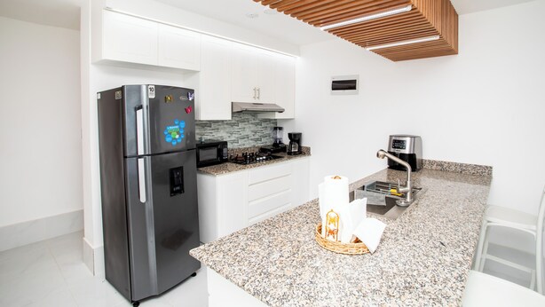 Una cocina moderna con armarios blancos, un refrigerador de acero inoxidable, una encimera de granito, un diseño de techo de madera y una cafetera.