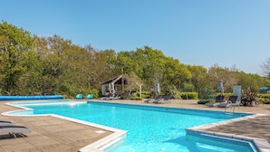 Una piscina rettangolare con bordo piastrellato, circondata da lettini e un padiglione coperto.