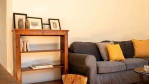 Een woonkamer met een grijze bank, een houten boekenkast en een geweven mand.