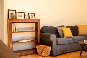 Ein Wohnzimmer mit grauem Sofa, einer Holzbibliothek und einem gewebten Korb.
