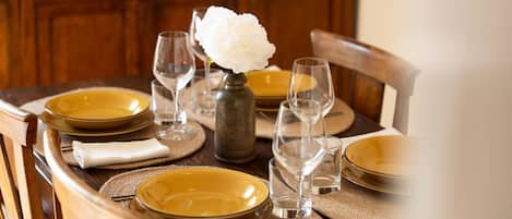 A dining table set with yellow plates, wine glasses, and a vase with a white flower.