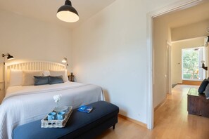 Ein Schlafzimmer mit Bett, Nachttisch und Schreibtisch. Ein Fenster bietet Blick auf Grünfläche.
