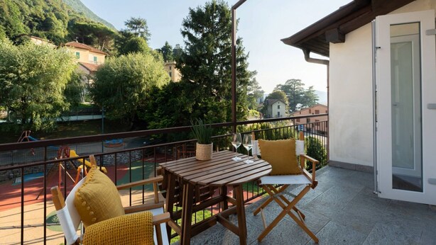 Een balkon met een tafel en stoelen, een uitzicht op een speeltuin en een berg op de achtergrond.