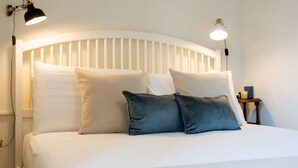 Een net opgemaakt bed met wit beddengoed en twee kussens, een wit hoofdbord en twee wandlampen.