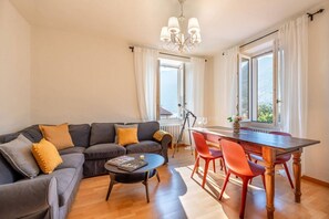 Ein Wohnzimmer mit einer Couch, einem Esstisch mit Stühlen, einem kleinen runden Tisch und einer Kandelaber.