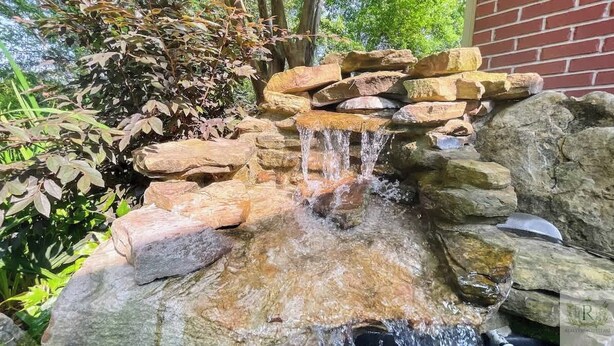 Ein kleiner Wasserfall mit Steinen und einer Ziegelwand im Hintergrund.