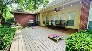 Eine überdachte Terrasse mit Ziegelaußenwand, Holzdeck, Gartenmöbeln und Lichterketten.