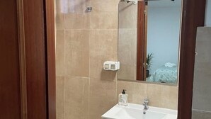 Une salle de bain avec un lavabo blanc, un miroir et un espace douche.