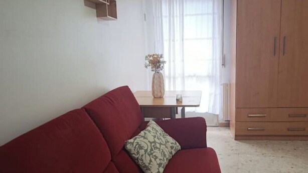 Un canapé rouge avec des coussins à motifs, un meuble en bois et une table sur laquelle est posé un vase.