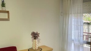 Une pièce avec un bureau en bois, un vase contenant des fleurs séchées, une chaise rouge et une fenêtre ornée de rideaux blancs.