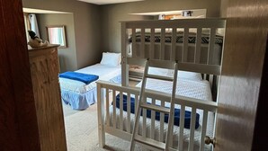 Un dormitorio con dos camas, una escalera y un ventanal pequeño.