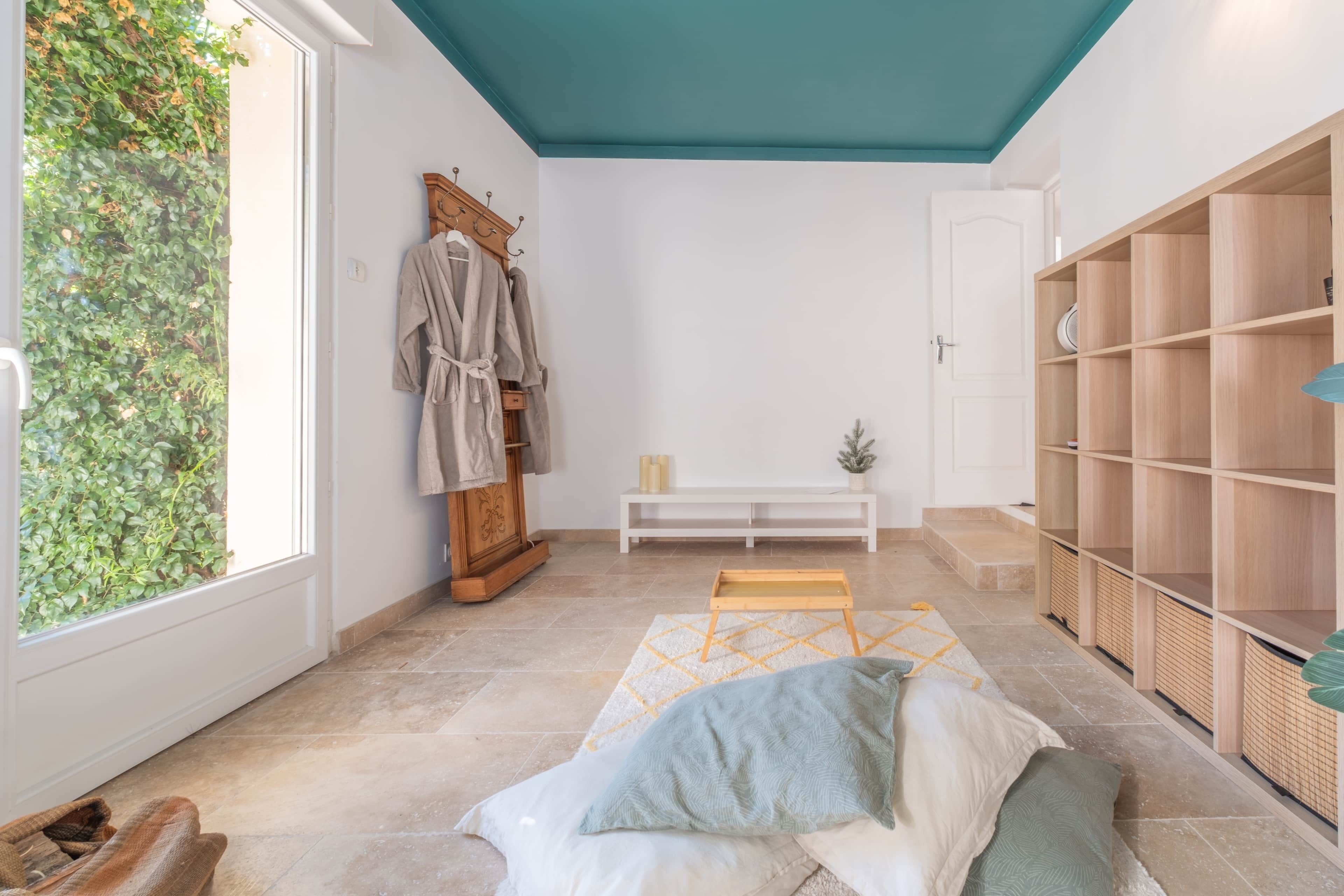 A room with a large window, a wooden bench, a white bench, and a wooden wardrobe.
