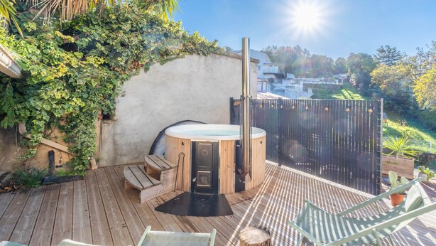 Une terrasse en bois avec un jacuzzi, des sièges d’extérieur et une vue sur un quartier résidentiel.